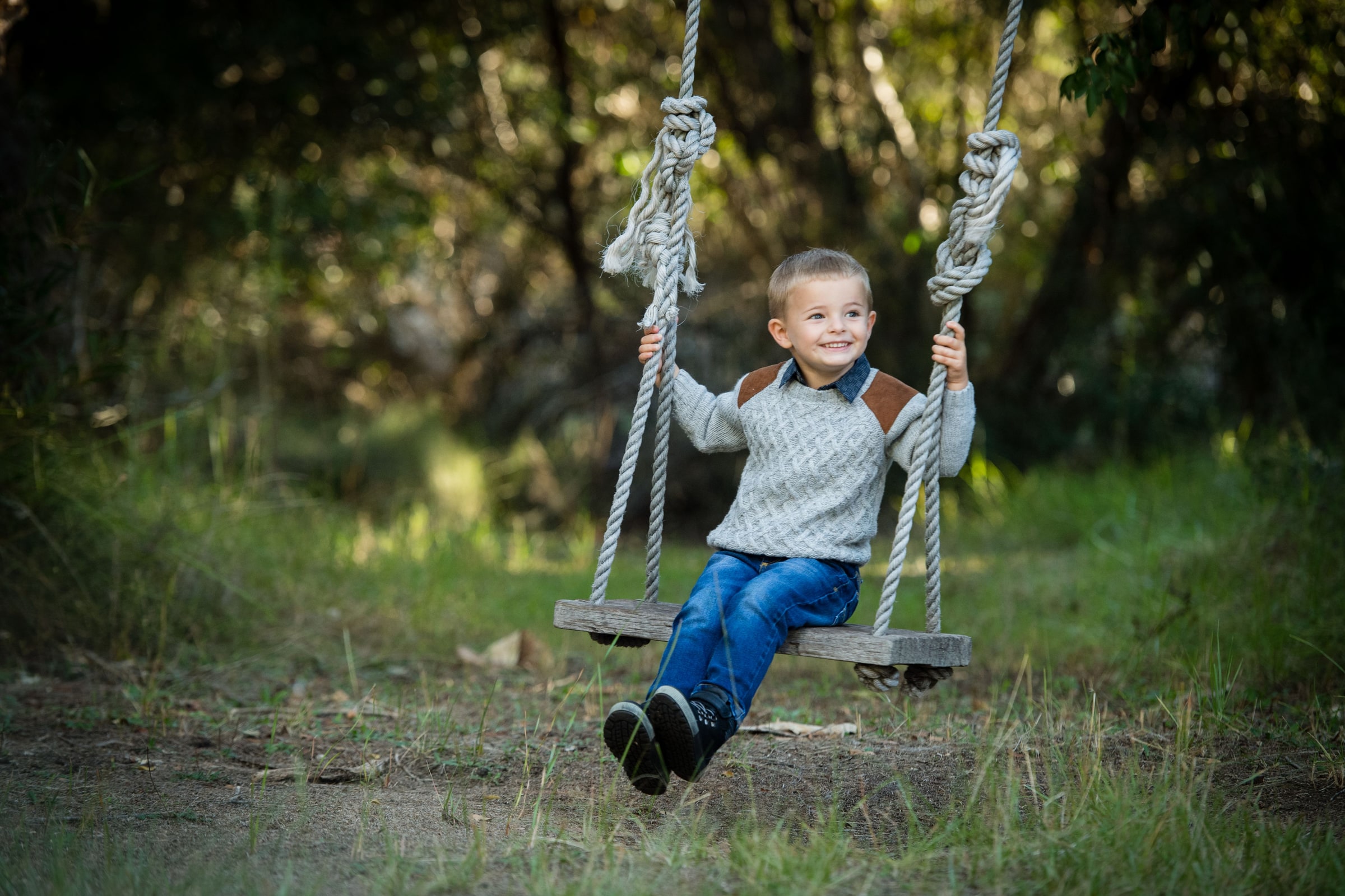 A little boy swinging in the dappled bushland light