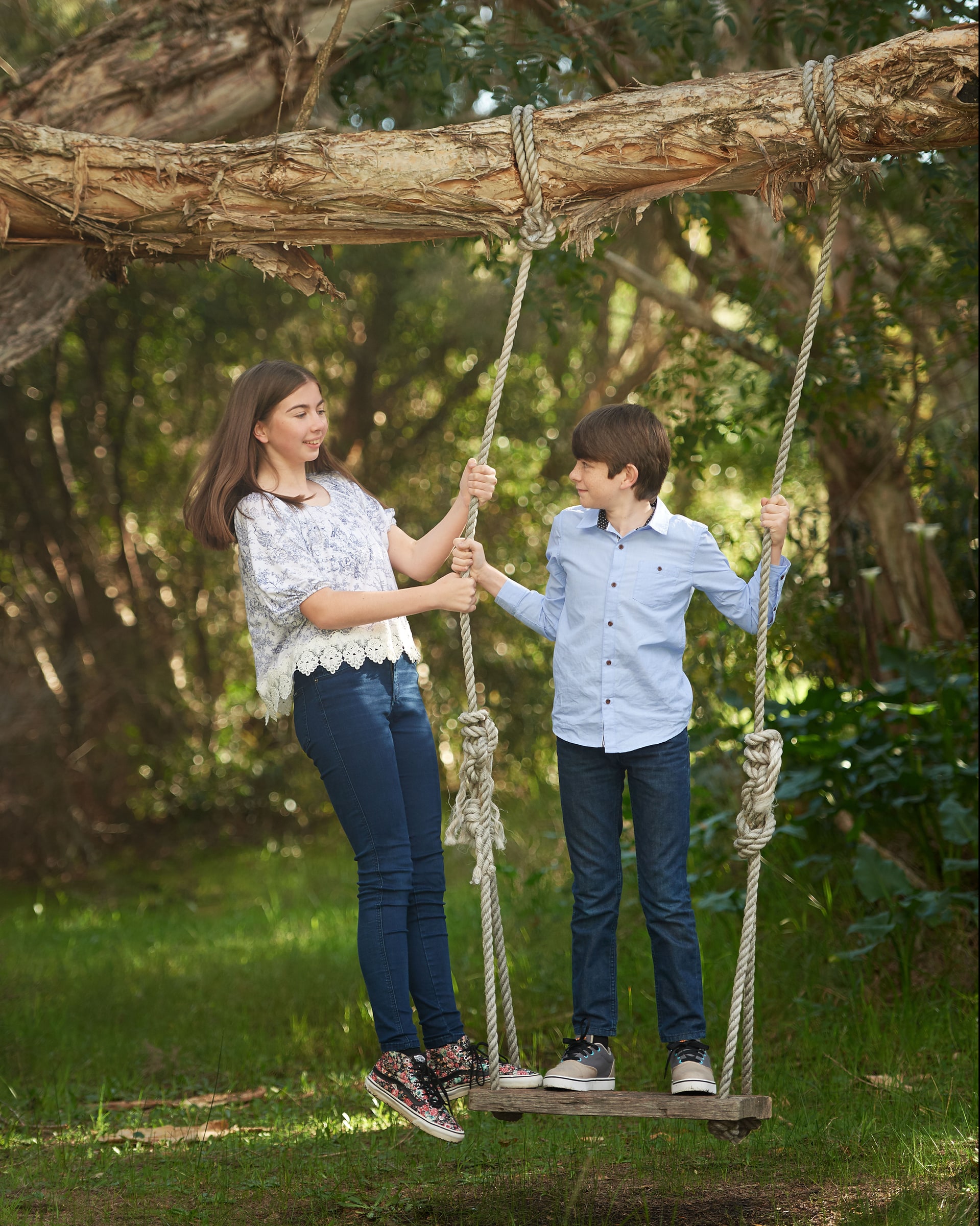 A sister and brother standing on the swing, holding the ropes