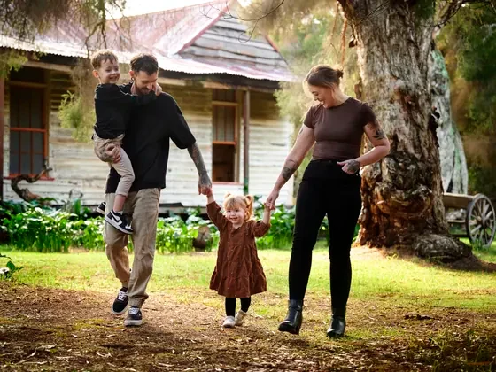Parents in black and tan with their daughter in brown walking past the cottage at Premier Studio
