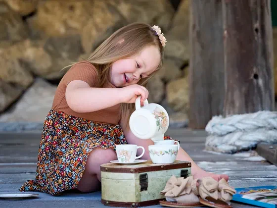 Little girl in a caramel top and floral skirt pouring tea on the deck at Premier Studio