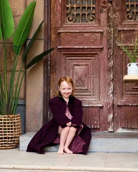 Little girl in a plum dress seated by the aged timber doors at Premier Studio