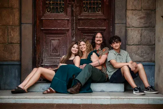 Family of four in emerald and teal seated on the red door steps at Premier Studio