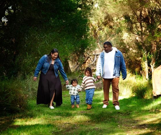Family of four in denim and cream walking hand in hand through the garden at Premier Studio