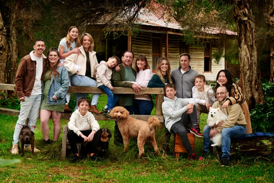 Extended family of twelve in cream, sage green and brown gathered before the cottage at Premier Studio