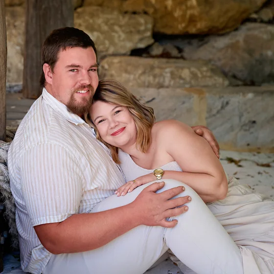 Couple in cream and a caramel-striped shirt seated against the limestone wall at Premier Studio