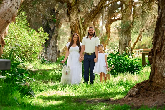 Family of three in white with dad in denim walking the bush path with their Samoyed at Premier Studio
