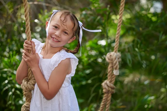 Little girl in a white lace dress holding the rope swing at Premier Studio