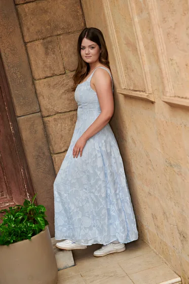 Young woman in a light blue maxi dress leaning against the limestone wall at Premier Studio
