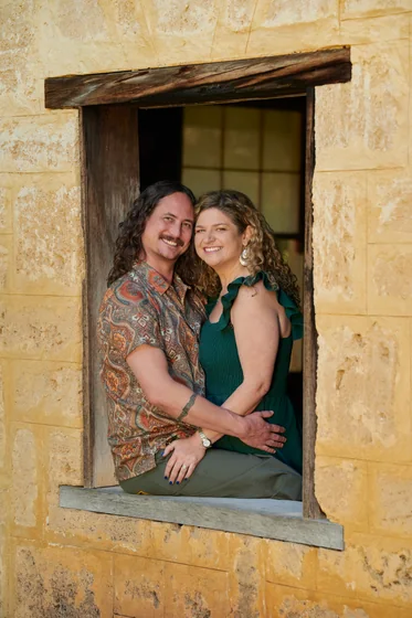 Couple in emerald green and an earthy floral shirt seated in the limestone window at Premier Studio