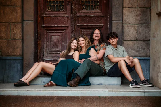 Family of four in emerald green, black and earthy florals seated before the red timber doors at Premier Studio