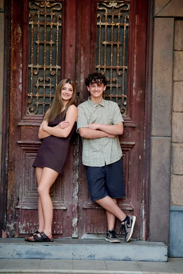 Teenage siblings in a black dress and sage shirt standing at the aged timber doors at Premier Studio