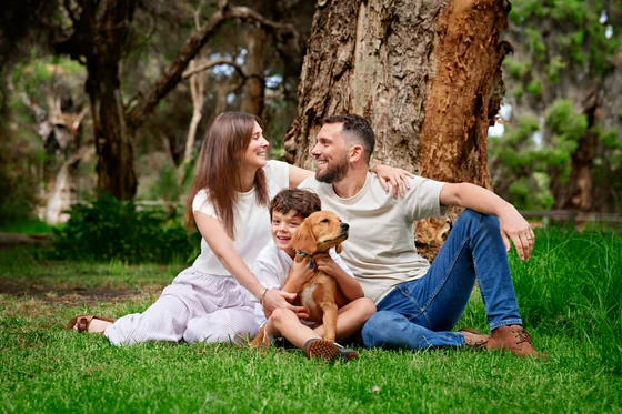 Parents in cream and denim with their son and puppy seated on the lawn at Premier Studio