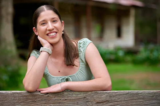 Young woman in a sage green top leaning on the timber fence at Premier Studio