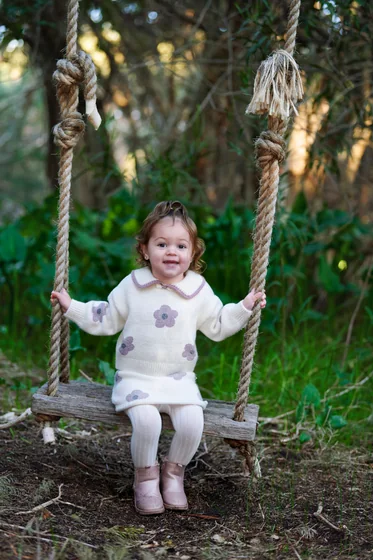 Little girl in a pink and cream knit swinging on the rope swing at Premier Studio