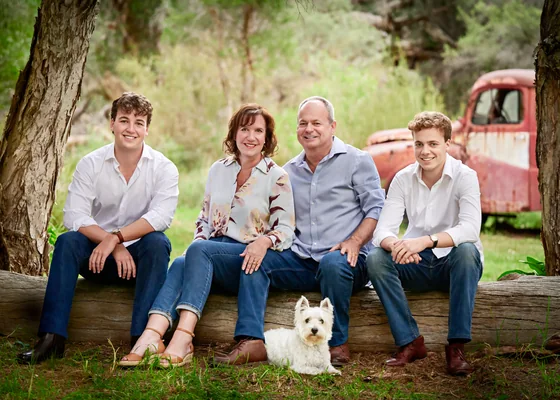 Family of four in blue and white shirts with their terrier seated on a log by the rust-red truck at Premier Studio