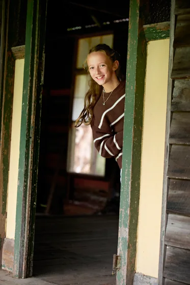 Young woman in a chocolate striped knit and brown trousers in the timber doorway at Premier Studio