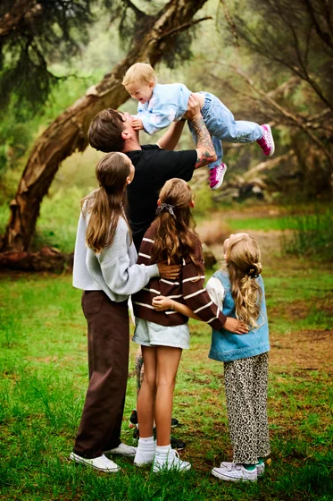 Family of five in chocolate brown, black, khaki and pale blue playing beneath the paperbark at Premier Studio