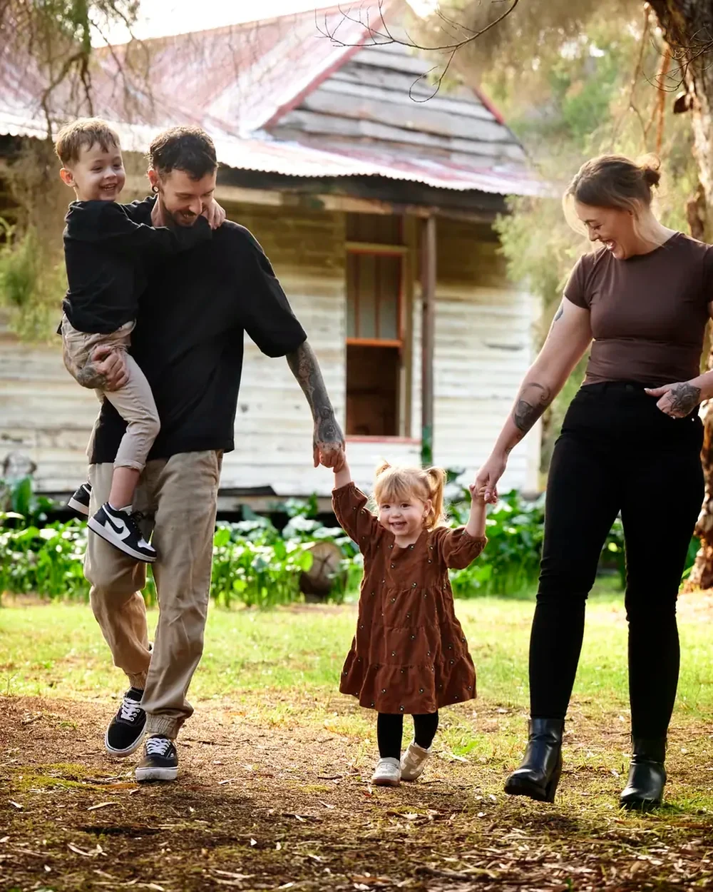 Parents in black and tan with their daughter in brown walking past the cottage at Premier Studio