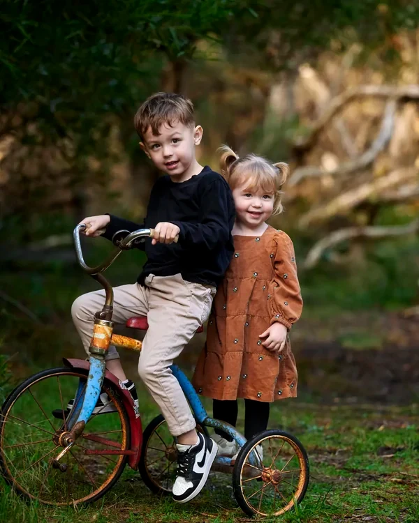 Brother in black and sister in a brown dress with a vintage bicycle in the bush at Premier Studio