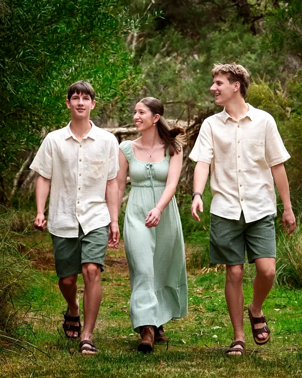 Mum in a sage dress with two sons in cream shirts and olive shorts walking through the bush at Premier Studio