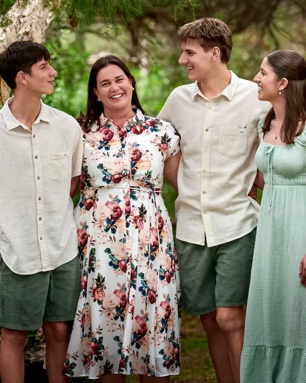 Family of four in sage green, cream and a soft floral dress among the trees at Premier Studio